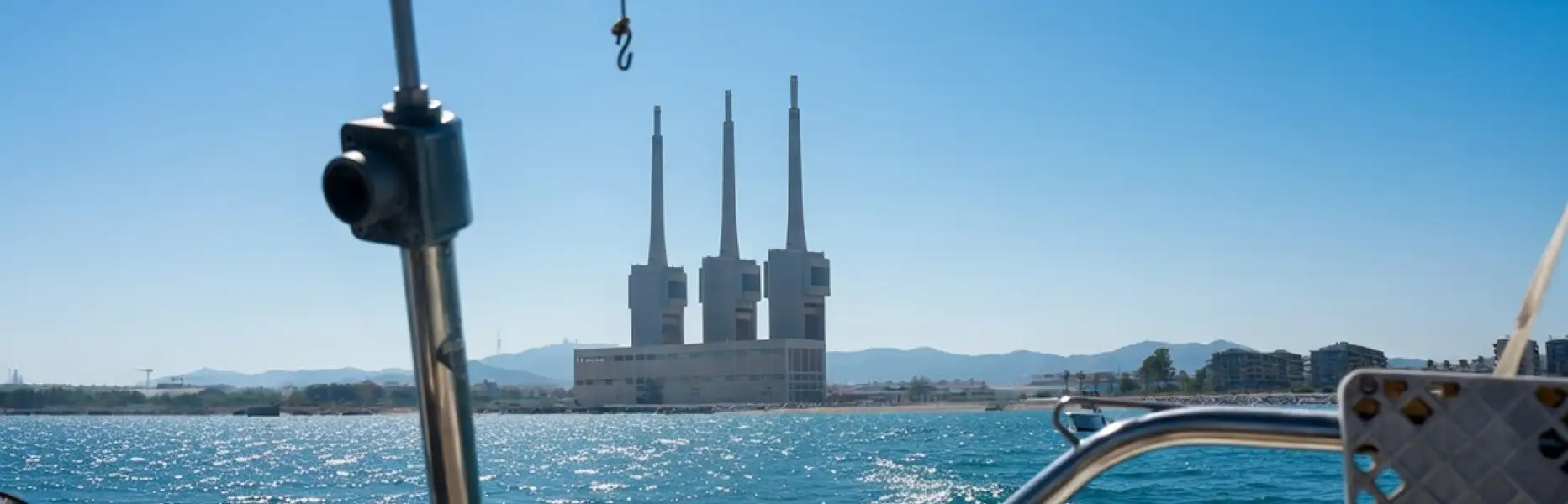 View from a sailing boat cruising off the coast of Barcelona with the blue sea and the towers of the Sant Adrià power station in the ba
