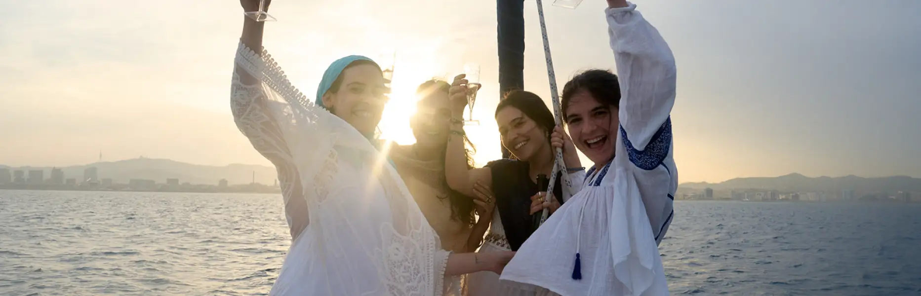 Group of friends toasting with cava at sunset on a boat in front of the Barcelona skyline