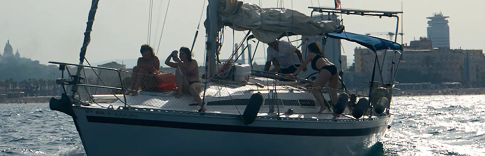 Gruppo di persone che si godono una gita in barca a vela al tramonto davanti alla costa di Barcellona