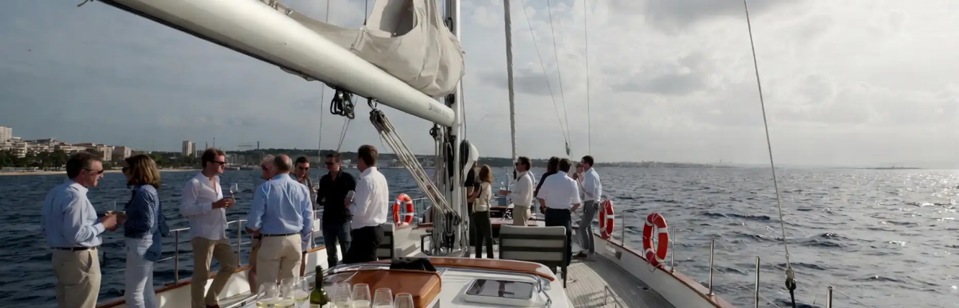 Grupo de personas disfrutando de un charter de lujo en velero con copas de vino sobre el mar
