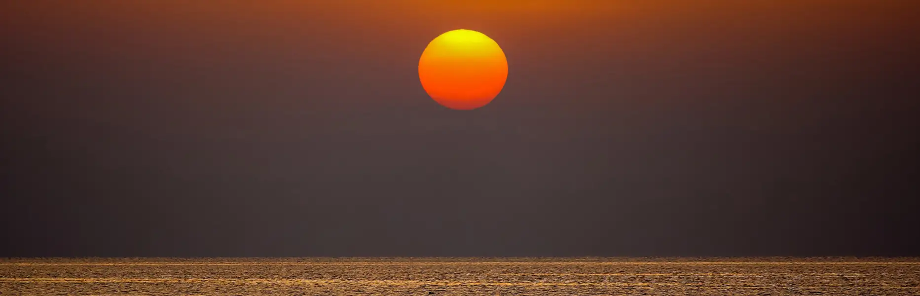Sol naciendo sobre el mar en calma durante un amanecer en Barcelona visto desde un velero
