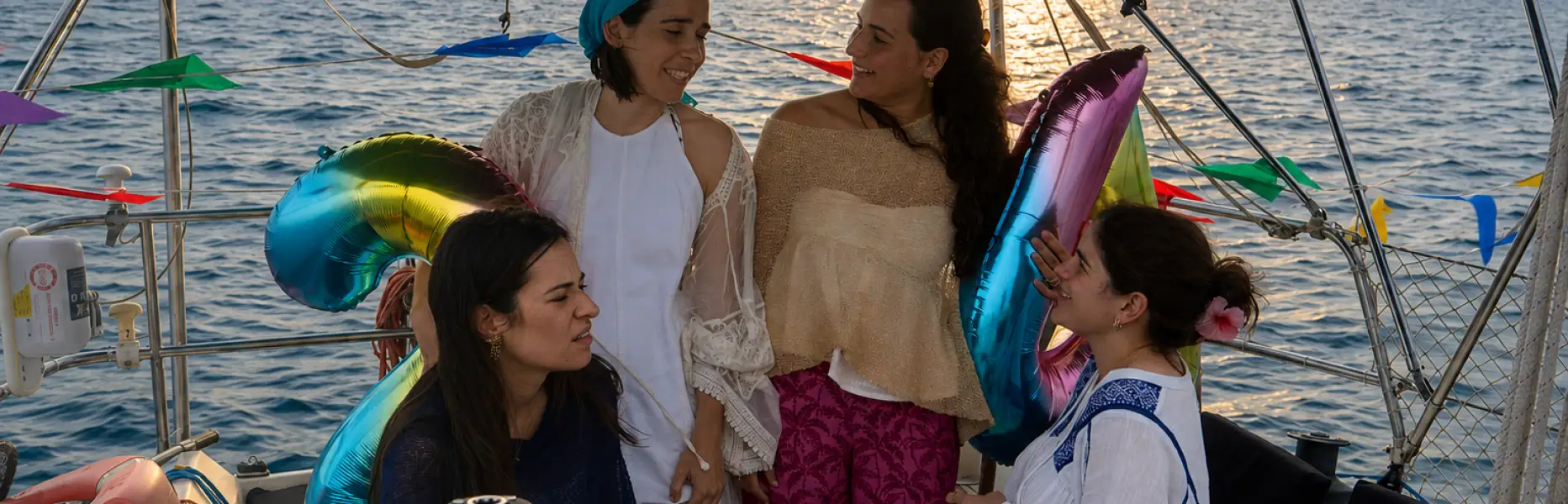 Group of friends celebrating a birthday on a private sailboat off the coast of Barcelona at sunset with balloons and decoratio