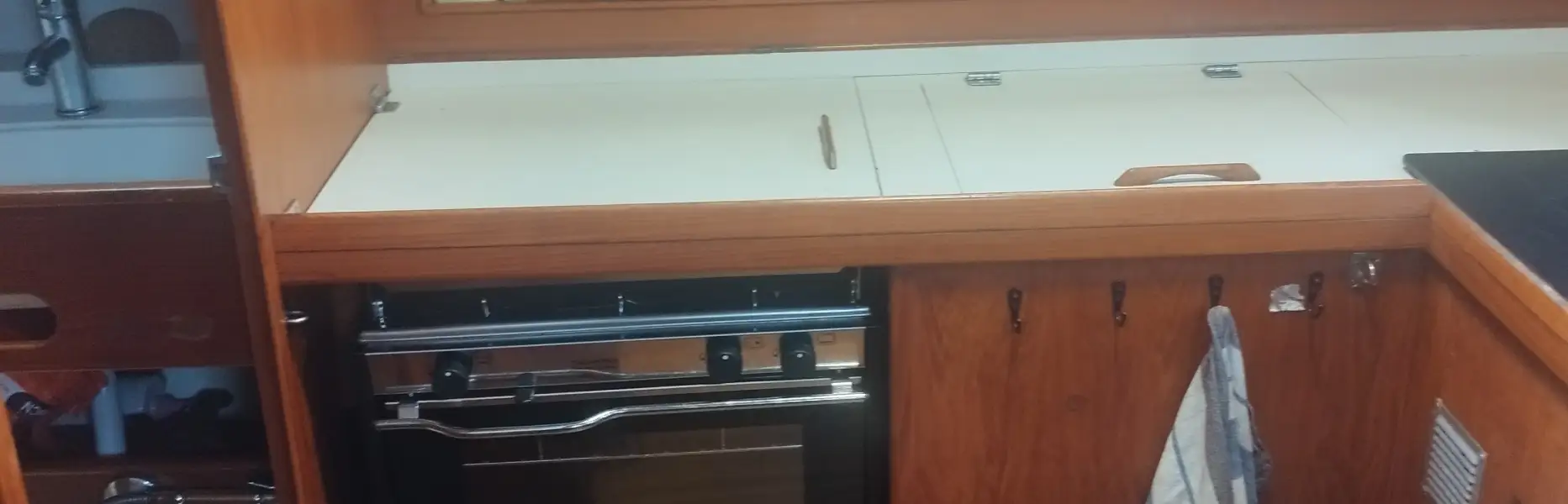 Cocina de madera totalmente equipada en el interior de un velero privado en Barcelona con horno, fregadero y toalla colgada