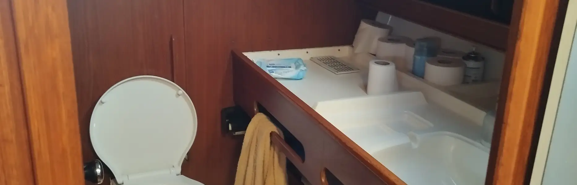 Salle de bain privée d’un voilier avec toilettes, lavabo et serviettes dans une cabine en bois