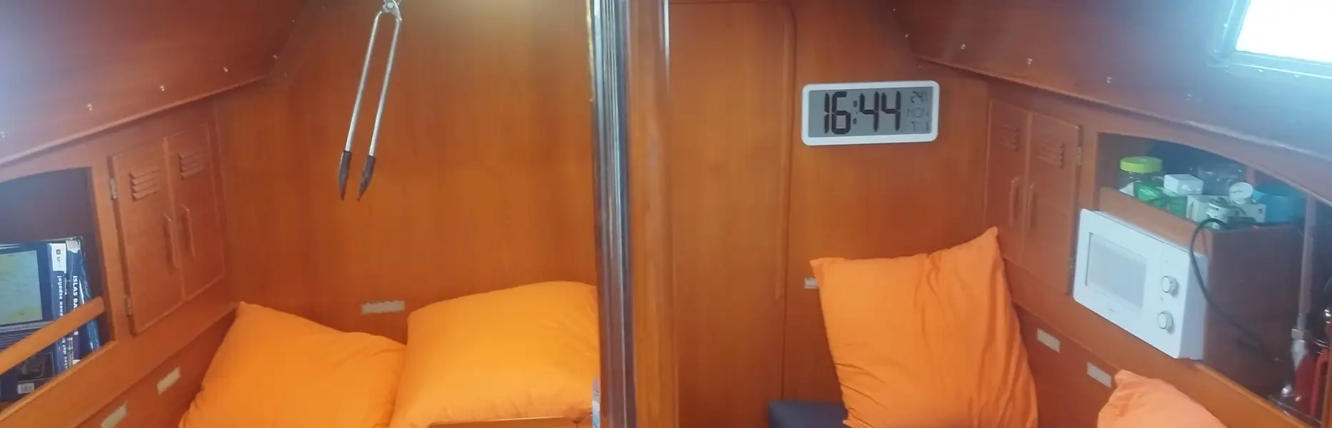 Intérieur de voilier avec salon en bois, coussins orange et horloge murale digitale, prêt pour l’expédition à l’éclipse totale de Soleil