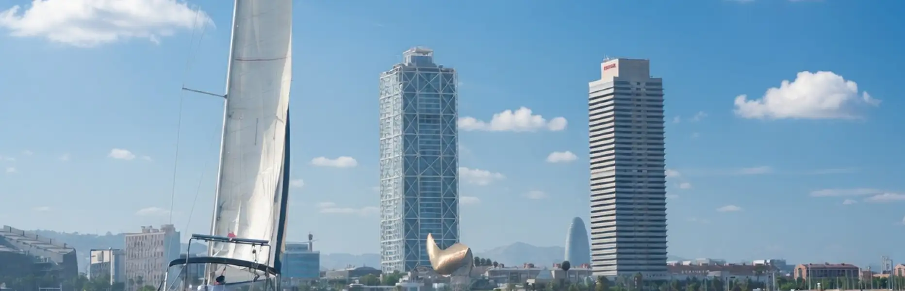 Velero de charter navegando en el mar frente al skyline de Barcelona en un día soleado