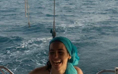 Giovane donna che sorride mentre naviga su una barca a vela privata al largo della costa di Barcellona