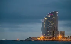 Vue de l’hôtel W de Barcelone au coucher du soleil, en bord de mer, avec les lumières allumées et un ciel nuageux