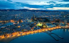 Aerial view of Barcelona at sunset with city lights and the illuminated coastline by the sea